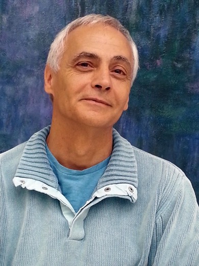 Portrait de Michel Piquemal, souriant devant une toile aux tons bleus.